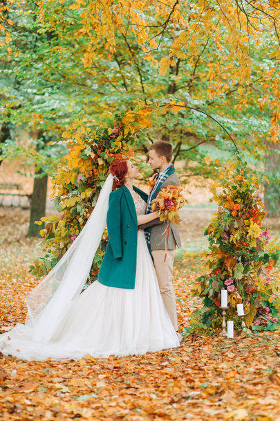 Szczęśliwych nowożeńców stojących przy łuku w dniu ślubu. Jesienny park. - Zdjęcie, obraz