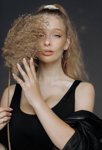 Portrait of a blonde girl in the studio with dry reed. She hides her face behind a branch of a reed. - Fotoğraf, Görsel