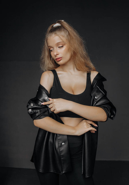 Portrait of a beautiful blonde with natural makeup in a black leather shirt on a dark background - Photo, Image