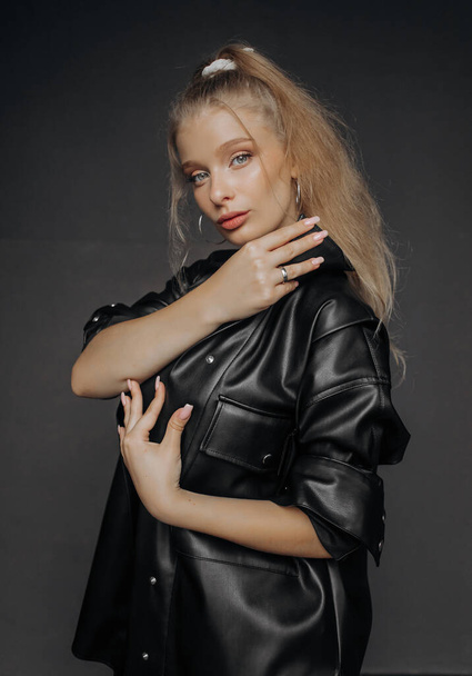 Porträt einer schönen Blondine mit natürlichem Make-up in einem schwarzen Lederhemd auf dunklem Hintergrund - Foto, Bild