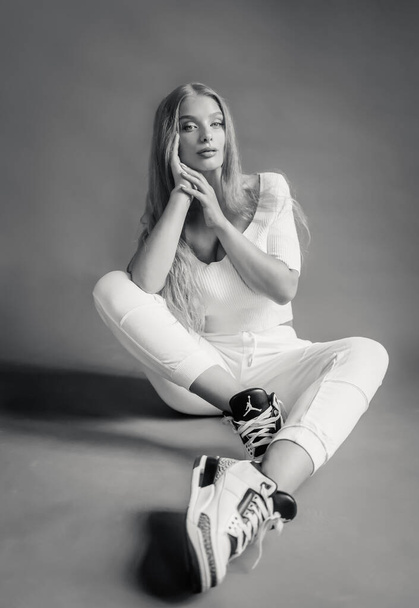 Black-white photo of a sexy blonde in white sportswear posing in the studio - Фото, изображение