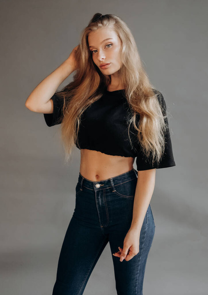 Gorgeous blonde in a black top and  jeans posing in the studio on a gray background - Foto, Bild