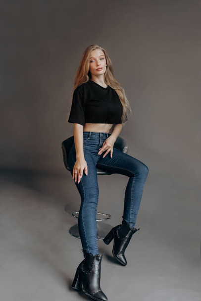 Luxury blonde dressed in a short top and jeans posing on a bar stool in the studio - Fotografie, Obrázek