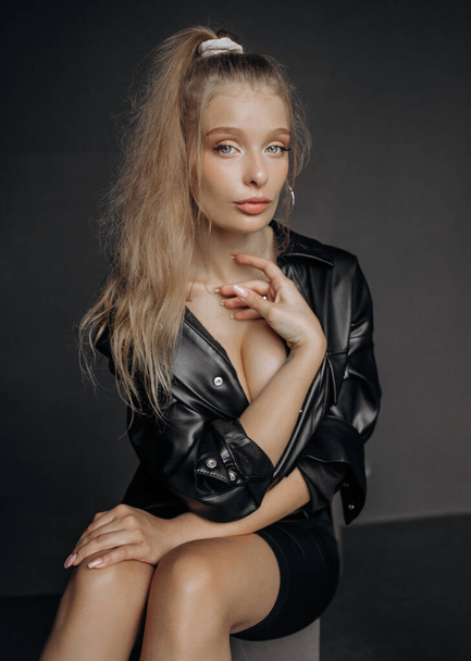Minimalistisches Porträt eines blonden weiblichen Modells auf grauem Hintergrund. stilvolle Kleidung, schwarzes Konzept im klassischen Stil - Foto, Bild