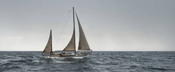 古い高価なヴィンテージの2人乗りの帆船(ヨール)が近くにあり、嵐の中オープン海を航海しています。帆を張れ。スポーツ、レガッタ、クルーズ、観光、レクリエーション、交通機関。パノラマビュー、海景 - 写真・画像