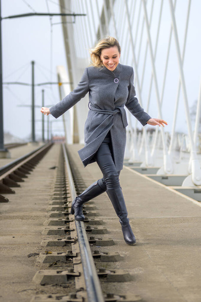 Femme adulte en vêtements tendance et élégant jouissant tout en courant et en jouant sur la voie ferrée sur le pont pendant la journée - Photo, image
