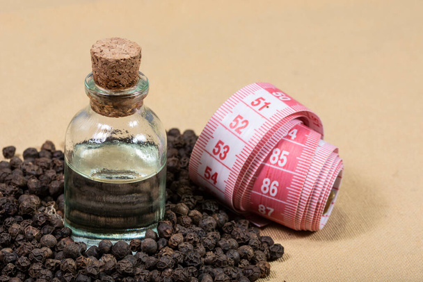 zwarte peper, een fles olie en een meetlint - Foto, afbeelding