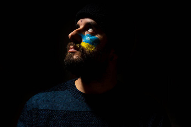 Stop war, conflict between Ukraine and Russia. A young Ukrainian with his face painted in the colors of the blue and yellow flag - 写真・画像