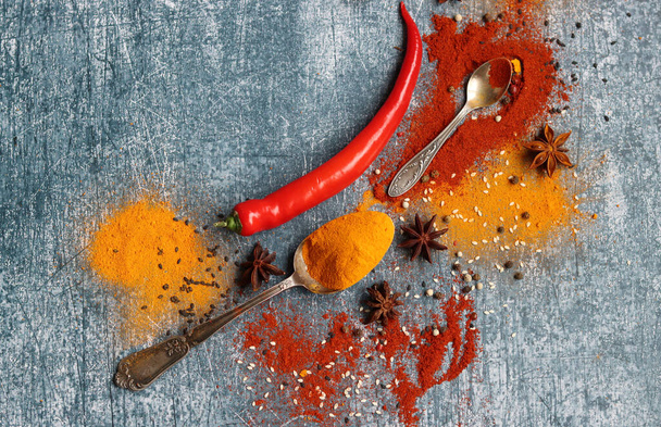 Chili pepper, paprika, turmeric, cinnamon, anise star and two vintage spoons on a table. Close up photo of aroma spices. grey textured background with copy space.  - Fotó, kép