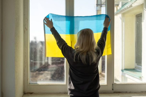 ウクライナの国旗を持つ難民女性です。愛国心、闘争、希望。ウクライナでの戦争。ウクライナの自由。戦争はない. - 写真・画像