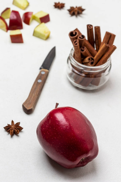 Ripe red apple on table. Cinnamon sticks in glass jar. Chopped apples and knife on table. Top view. White background - Foto, Imagen