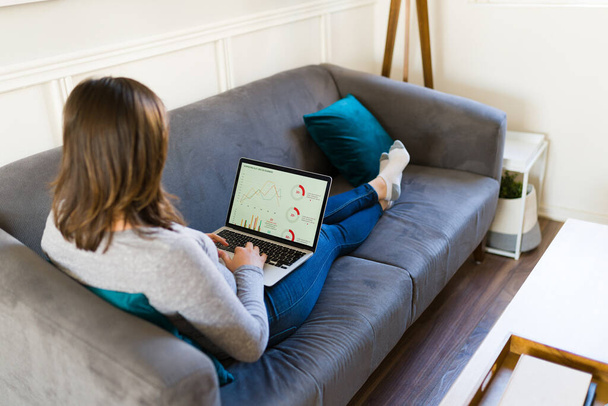 Mujer joven gen z mirando las cartas comerciales e invertir en acciones en línea mientras trabaja en casa  - Foto, imagen