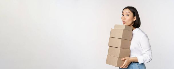 Ritratto di giovane donna asiatica che tiene scatole, trasportare merci di consegna. Imprenditore coreano assemblare ordine, in piedi voer sfondo bianco - Foto, immagini