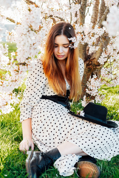 Portrait of a sensual young brunette in a dress with a flower of a pink blossoming tree. Generation Z girl enjoys the spring mood on a sunny day. Vertical map. Selective focus, copy space - Foto, immagini