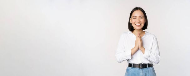 Portrait of happy asian girl laughing and smiling, showing thank you, namaste gesture, grateful for smth, standing over white background - Foto, immagini