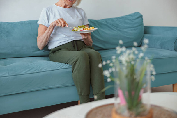 Mulher aposentada tomando café da manhã no sofá em casa - Foto, Imagem