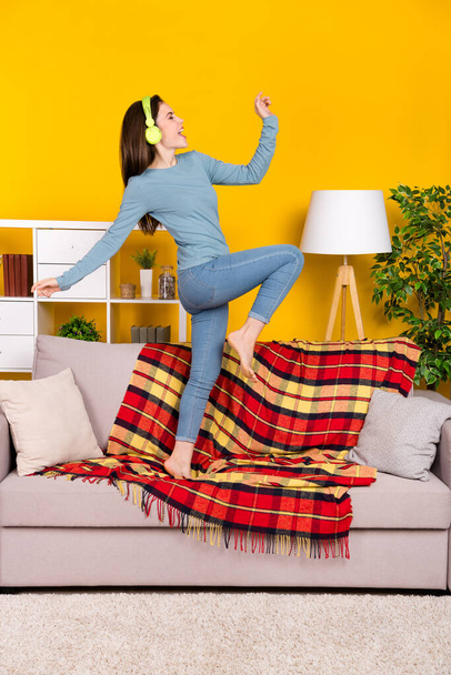 Full length vertical portrait of childish cheerful person stand sofa listen music isolated on yellow color background - Foto, immagini