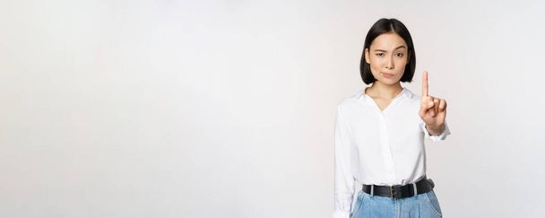 No. Young serious and confident asian woman showing stop, one finger gesture, taboo sign, standing over white background - Photo, Image