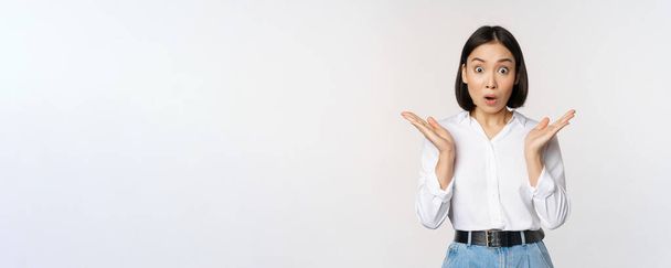 Immagine di asiatica modello femminile guardando sorpreso, fissando stupito, reagendo a sorpresa grande notizia, in piedi su sfondo bianco - Foto, immagini