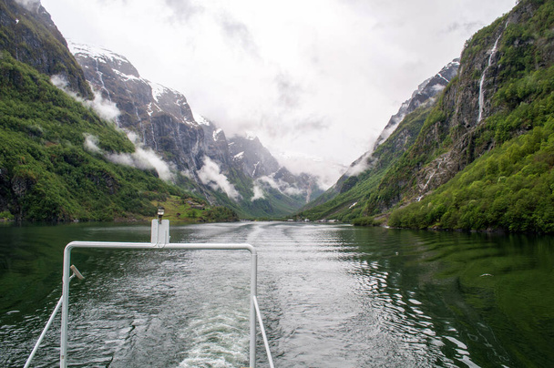 Sognefjord, Norvegia - 21 maggio 2016: Vista dalla barca sull'acqua in una valle profonda (fiordo) intorno alla quale sorgono alte colline verdi e sopra di loro ci sono nuvole - Foto, immagini
