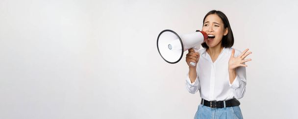 Image of young woman, korean activist, recruiter screaming in megaphone, searching, shouting at loudspeaker, standing over white background - Фото, зображення