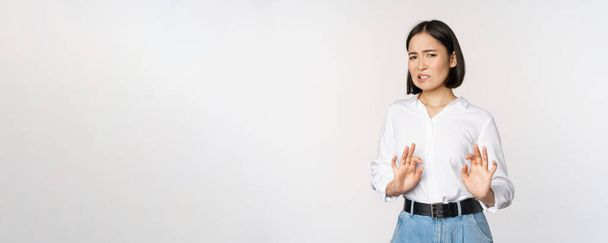 No thank you. Young disgusted asian woman declining proposal, shaking hands and step back, looking with dislike, rejecting offer, standing over white background - Photo, Image