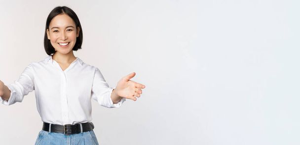 Image de femme asiatique souriante accueillant les clients, femme d'affaires étirant les mains ouvertes, salutation, debout sur fond blanc - Photo, image
