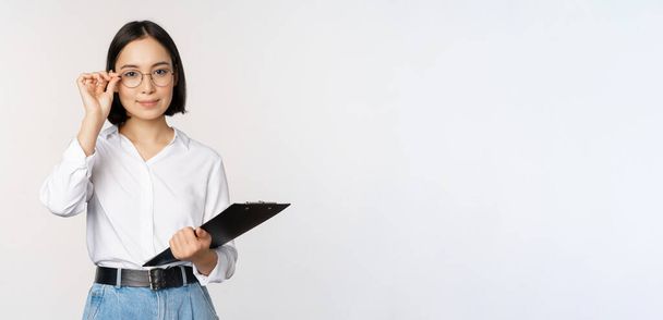 Genç bir kadın, gözlüklü bir ofis çalışanı, elinde bir pano, profesyonel gibi görünüyor, beyaz arka planda duruyor. - Fotoğraf, Görsel