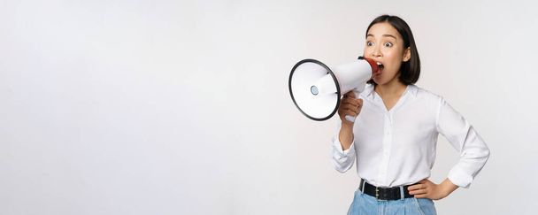 Image of young woman, korean activist, recruiter screaming in megaphone, searching, shouting at loudspeaker, standing over white background - 写真・画像