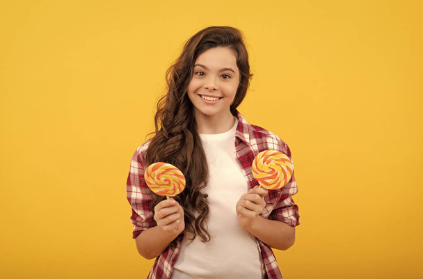 glücklich Teenager-Mädchen mit lockigem Haar halten Lutscher Karamell-Bonbons auf gelbem Hintergrund, Karamell-Shop. - Foto, Bild