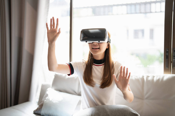 Excite asian woman playing online game with vr glasses and controller at her home - Photo, Image