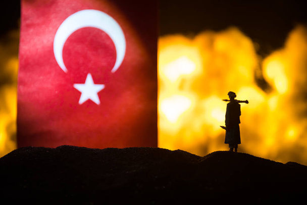 Turkey small flag on burning dark background. Concept of crisis of war and political conflicts between nations. Silhouette of armed soldier against a Turkish flag. Selective focus - Photo, Image