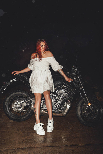 Redhead woman with black motorbike outdoors at night - Photo, Image