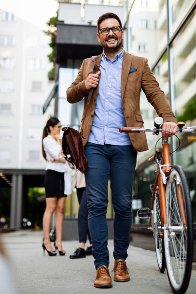 Portrait of happy fit young business man with bicycle in modern city outdoors. - Fotografie, Obrázek
