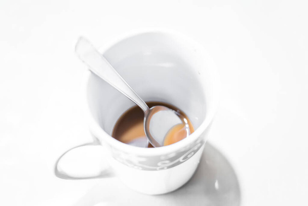 Close up of white coffee cup against white background with spoon and brown coffee, Germany - Photo, image