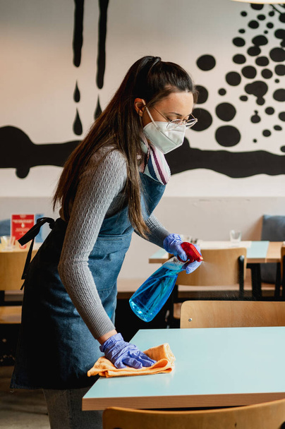 vista lateral joven camarera latina mesa de limpieza en restaurante con spray y toallita. - Foto, imagen