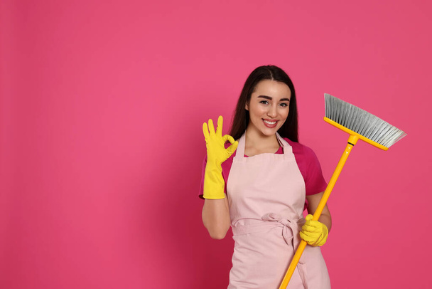 Beautiful young woman with broom showing OK gesture on pink background. Space for text - Fotografie, Obrázek