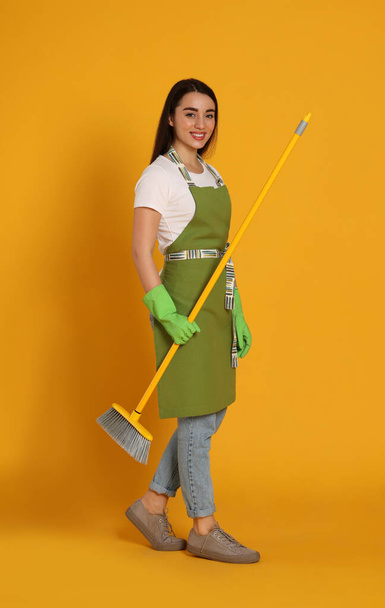 Beautiful young woman with broom on yellow background - 写真・画像
