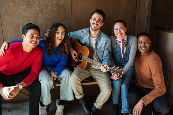 Mixed group of young friends looking at the camera posing with happy and smiling faces while playing guitar. - Foto, imagen