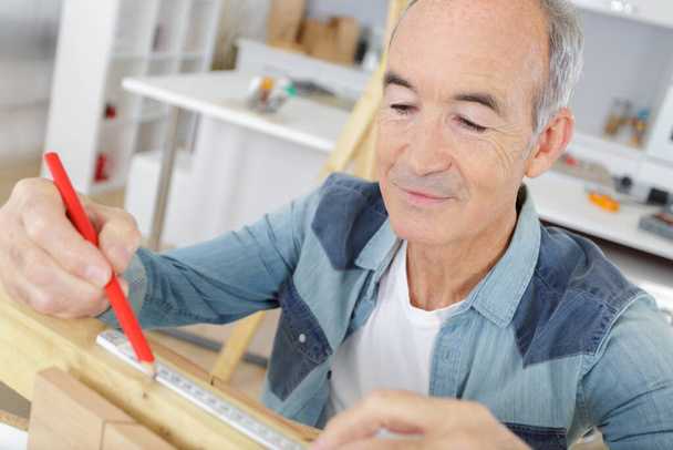 senior handyman drawing line on wood with a pencil - Valokuva, kuva