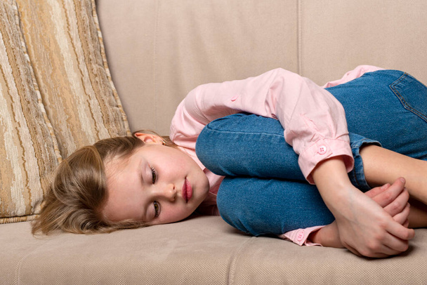 Evdeki kanepede uzanmış küçük bir kızın bir şeye üzülmesi. - Fotoğraf, Görsel