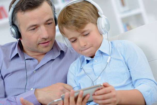 Man and boy wearing headphones, looking at electronic device - Foto, Imagem