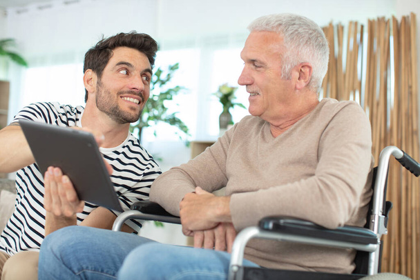cheerful disabled retired man sitting in wheelchair near bearded son - Φωτογραφία, εικόνα