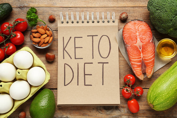 Notebook with phrase Keto Diet and different products on wooden table, flat lay - 写真・画像