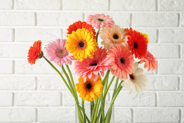 Bouquet of beautiful colorful gerbera flowers in vase against white brick wall - Foto, afbeelding