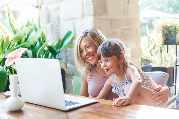 Ξανθιά γυναίκα και χαριτωμένη μικρή κόρη της video-chat με τους φίλους ή τους συγγενείς τους χρησιμοποιώντας φορητό υπολογιστή - Φωτογραφία, εικόνα