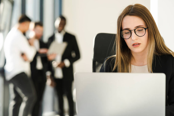 Secrétaire féminine travaille sur un ordinateur portable dans le bureau et ses collègues en arrière-plan - Photo, image