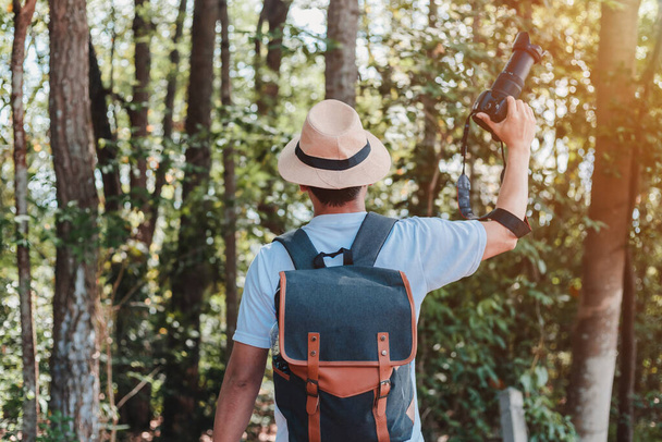 ハンドバッグ、水ボトル、カメラを持っている男性観光客が森を歩く. - 写真・画像