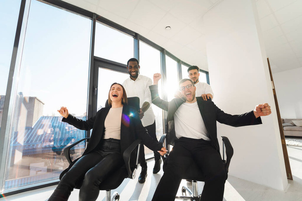 Büroangestellte mit mehreren Rassen sitzen in einer Pause auf Stühlen und freuen sich über den Erfolg des Unternehmens - Foto, Bild