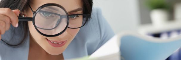 Woman looking at documents in folder through magnifying glass - Foto, Imagen